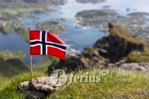 Norwegian Flag on the Nonstinden mountain. Blurred in the background the view down to Ballstad, Vestvågøya island, Lofoten Islands, Norway