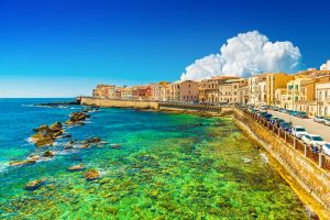 Beautiful cityscape of Ortygia (Ortigia), the historical center of Syracuse, Italy. Skyline of a European coastal town with turquoise transparent water and picturesque clouds in the sky